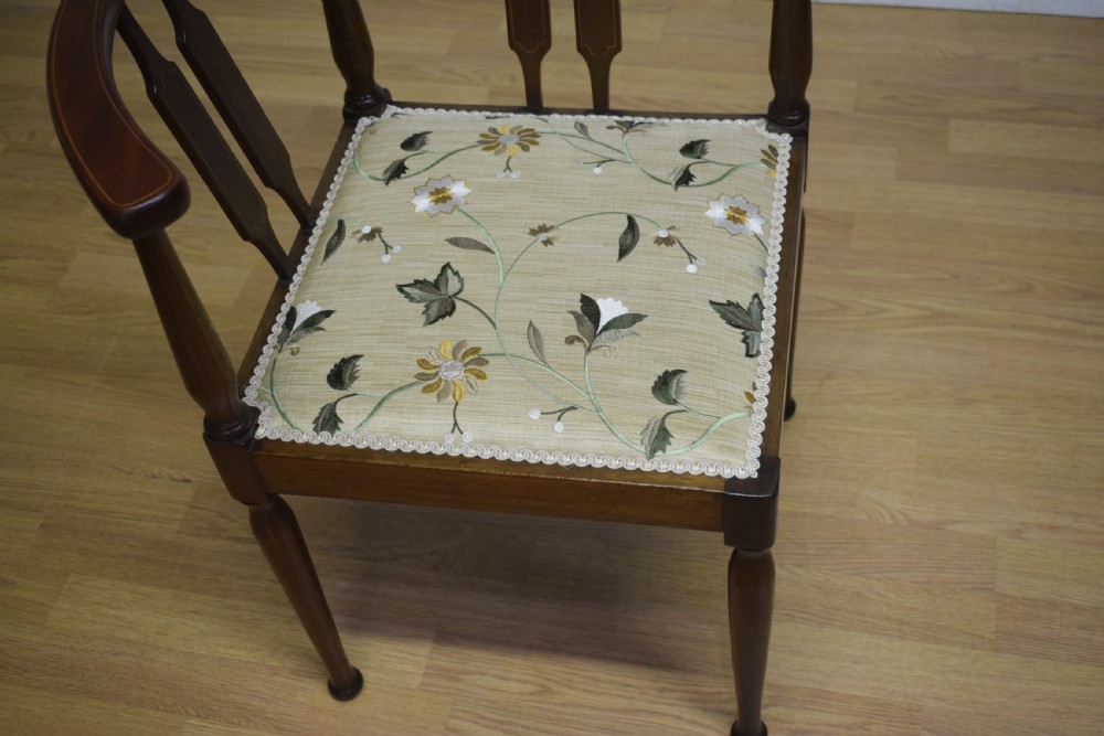 An Edwardian mahogany corner chair featuring a curved top rail with fan inlay, turned spindles, and a floral upholstered square seat. View V