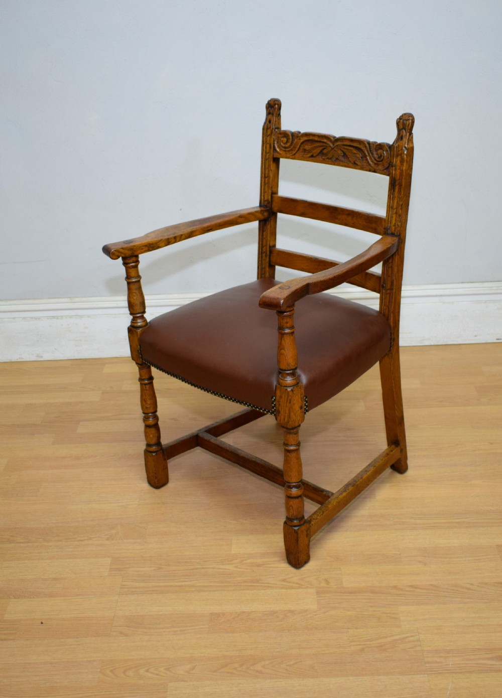 A carved oak armchair featuring a brown leather seat with stud detailing, turned front legs, and carved crest rail on the backrest. View II