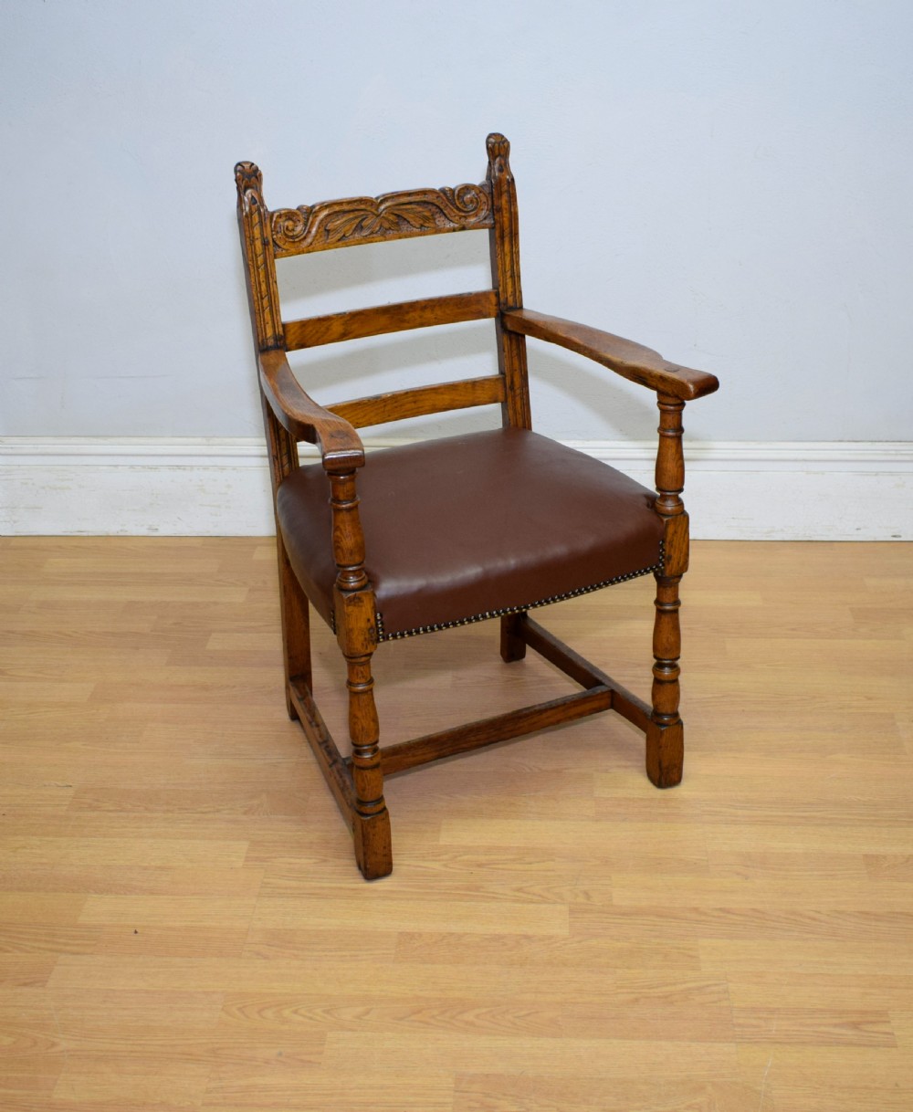 A carved oak armchair featuring a brown leather seat with stud detailing, turned front legs, and carved crest rail on the backrest. View III