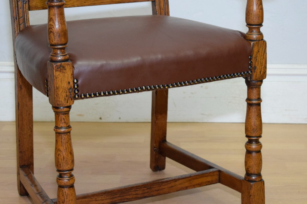 A carved oak armchair featuring a brown leather seat with stud detailing, turned front legs, and carved crest rail on the backrest. View VI