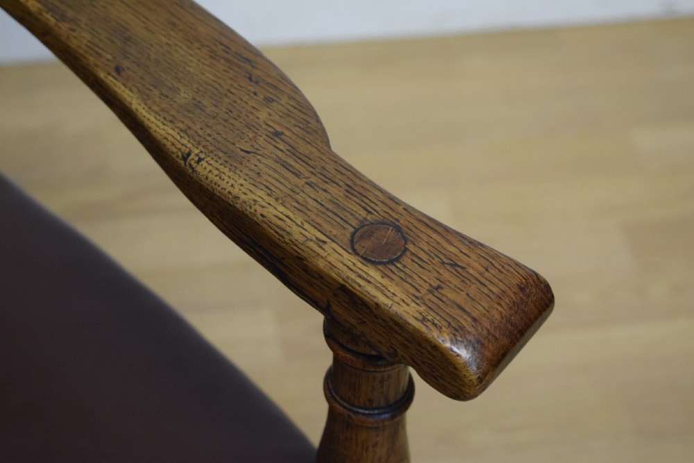 A carved oak armchair featuring a brown leather seat with stud detailing, turned front legs, and carved crest rail on the backrest. View IX