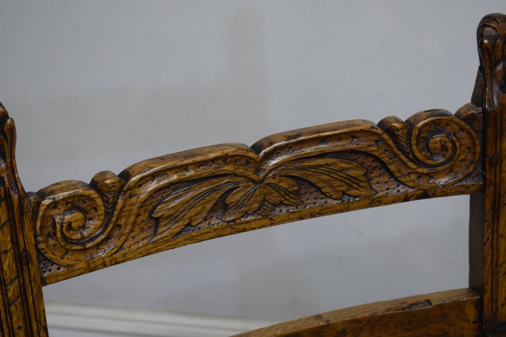 A carved oak armchair featuring a brown leather seat with stud detailing, turned front legs, and carved crest rail on the backrest. View XI