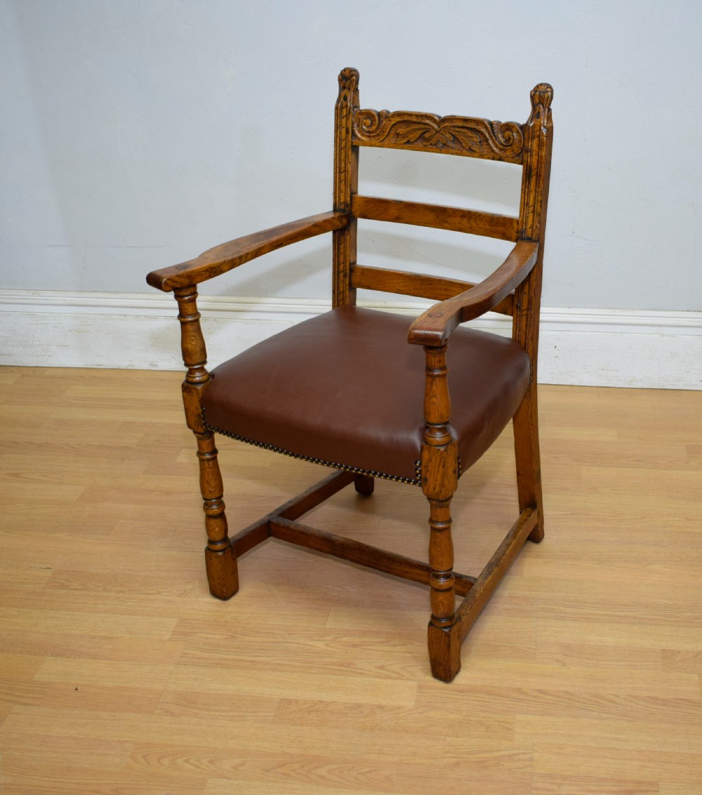 A carved oak armchair featuring a brown leather seat with stud detailing, turned front legs, and carved crest rail on the backrest. View XII