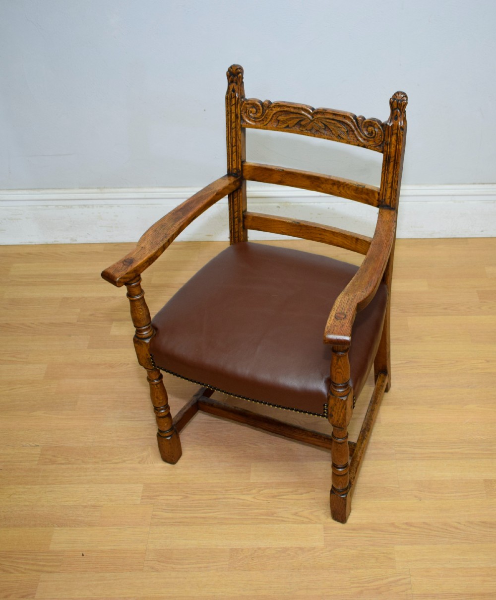 A carved oak armchair featuring a brown leather seat with stud detailing, turned front legs, and carved crest rail on the backrest. View XIII