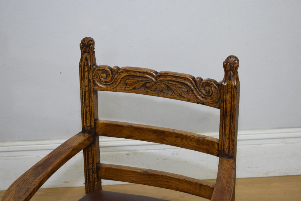 A carved oak armchair featuring a brown leather seat with stud detailing, turned front legs, and carved crest rail on the backrest. View XIV