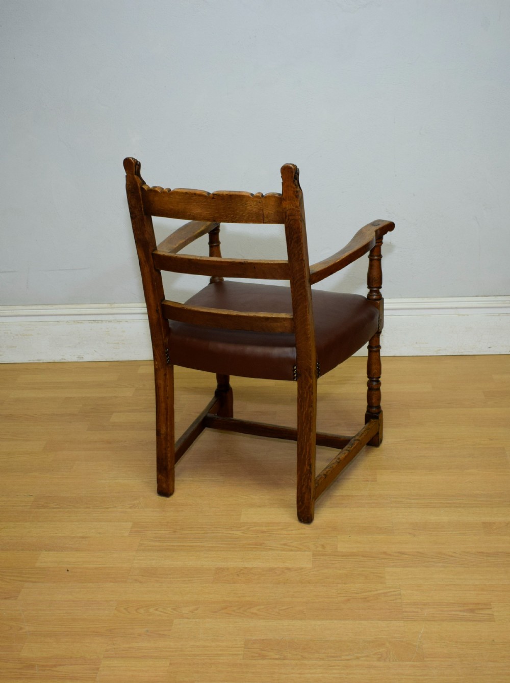 A carved oak armchair featuring a brown leather seat with stud detailing, turned front legs, and carved crest rail on the backrest. View XVI