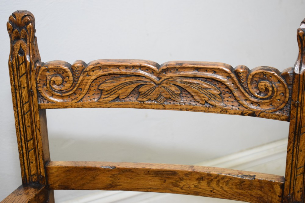 A carved oak armchair featuring a brown leather seat with stud detailing, turned front legs, and carved crest rail on the backrest. View XVIII
