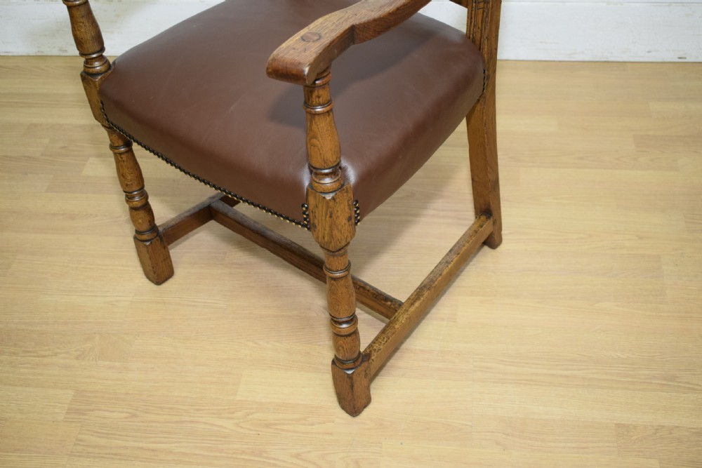 A carved oak armchair featuring a brown leather seat with stud detailing, turned front legs, and carved crest rail on the backrest. View XIX