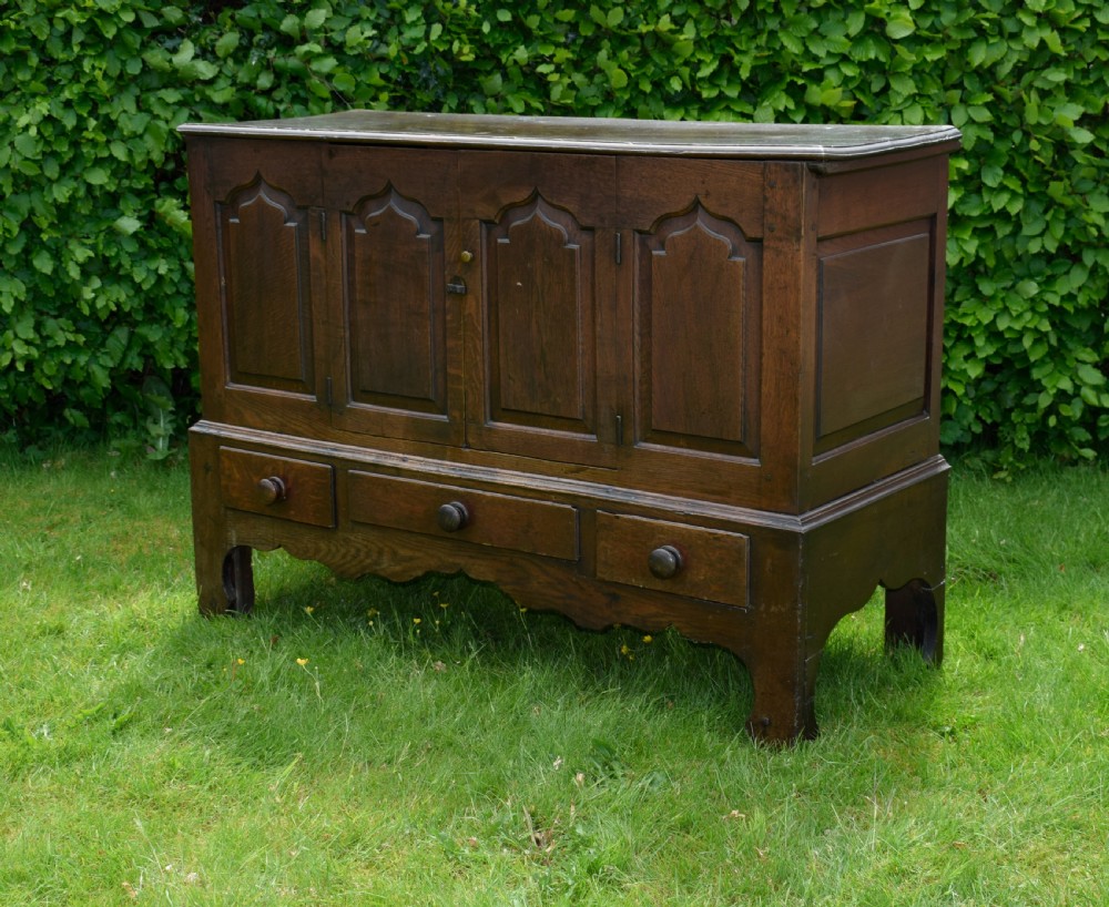 A 17th-century style dark oak court cupboard with four arched fielded panel doors over three drawers fitted with turned wooden knobs.