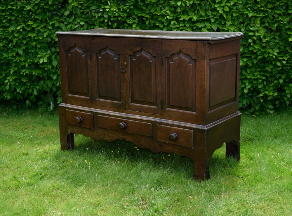 A 17th-century style dark oak court cupboard with four arched fielded panel doors over three drawers fitted with turned wooden knobs. View II