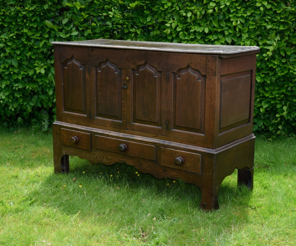 A 17th-century style dark oak court cupboard with four arched fielded panel doors over three drawers fitted with turned wooden knobs. View III
