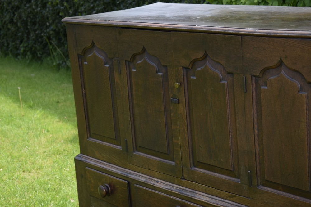 A 17th-century style dark oak court cupboard with four arched fielded panel doors over three drawers fitted with turned wooden knobs. View IX