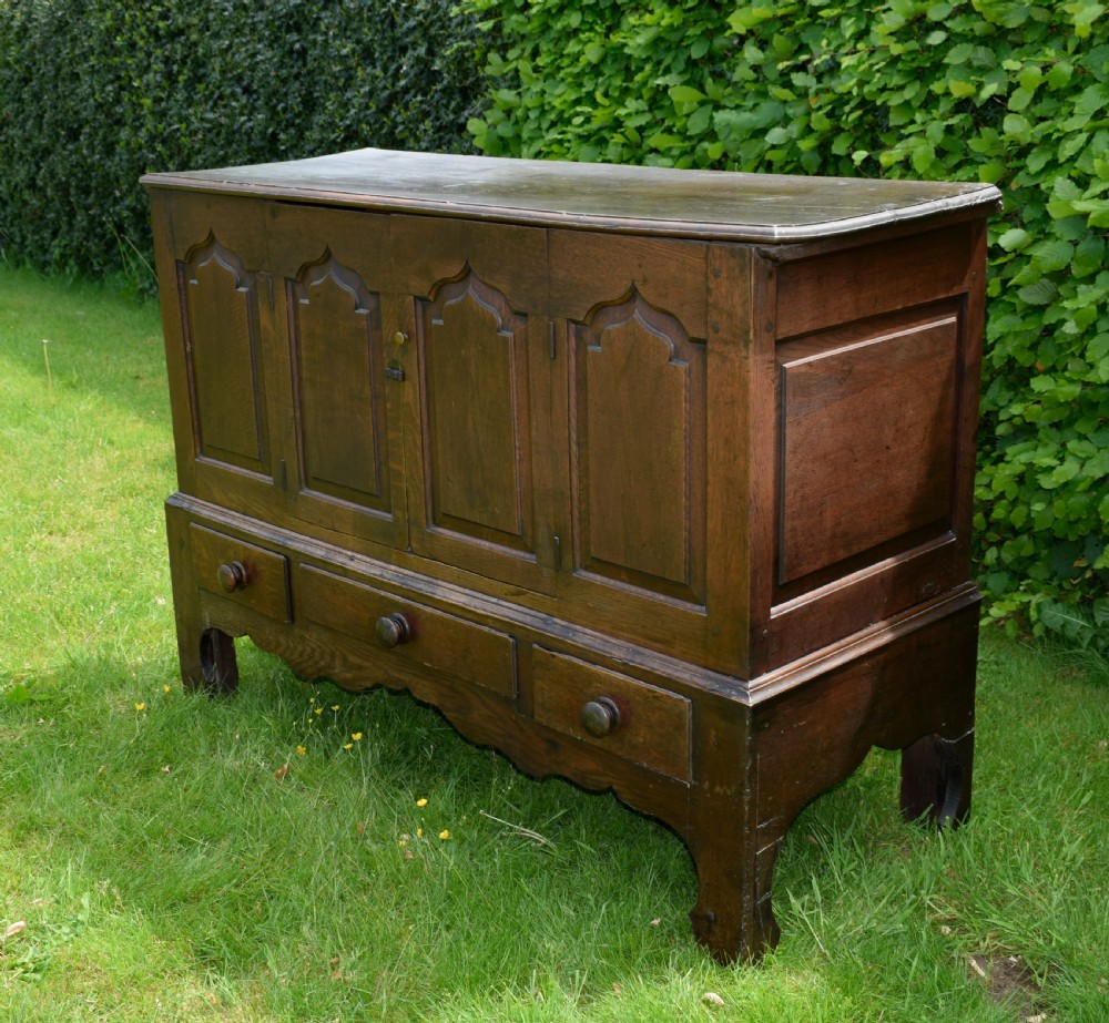 A 17th-century style dark oak court cupboard with four arched fielded panel doors over three drawers fitted with turned wooden knobs. View X