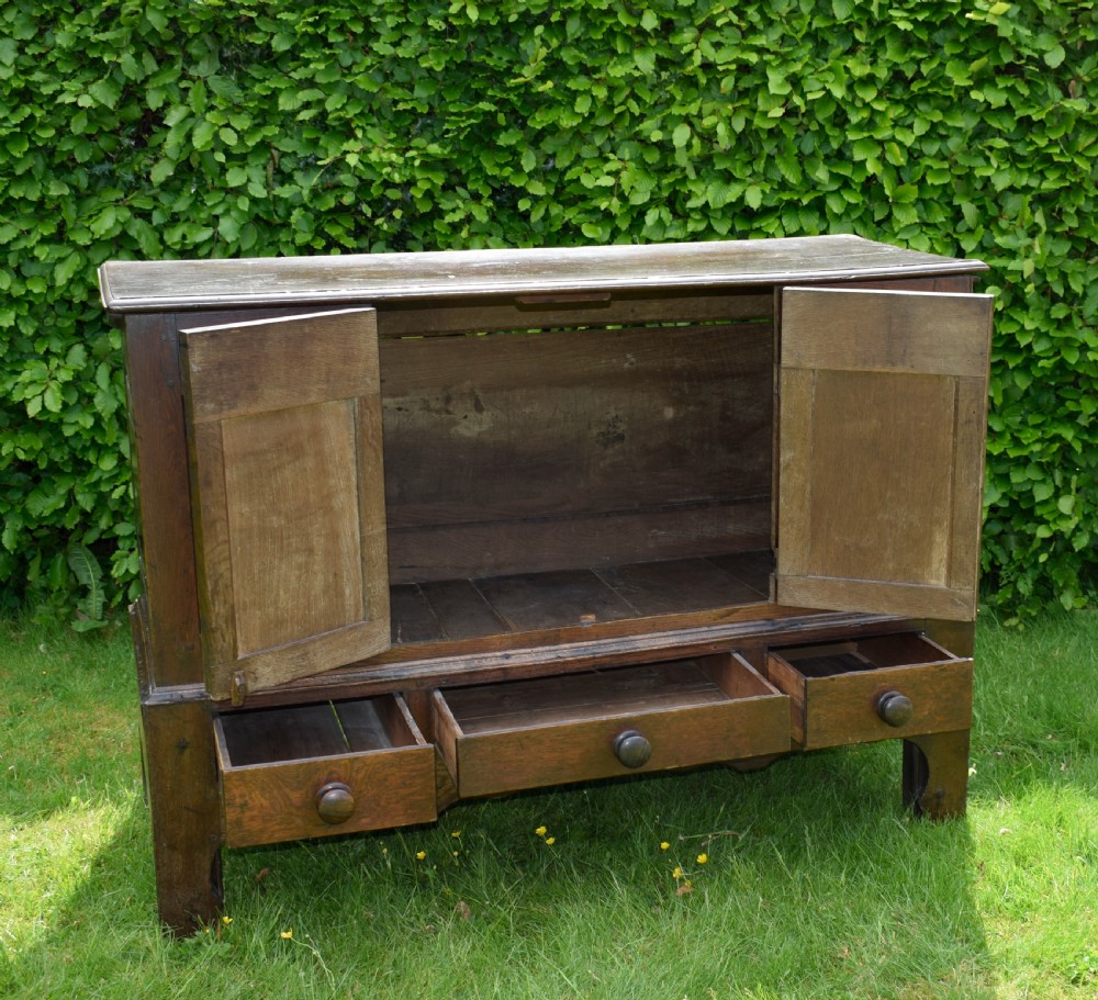 A 17th-century style dark oak court cupboard with four arched fielded panel doors over three drawers fitted with turned wooden knobs. View XI
