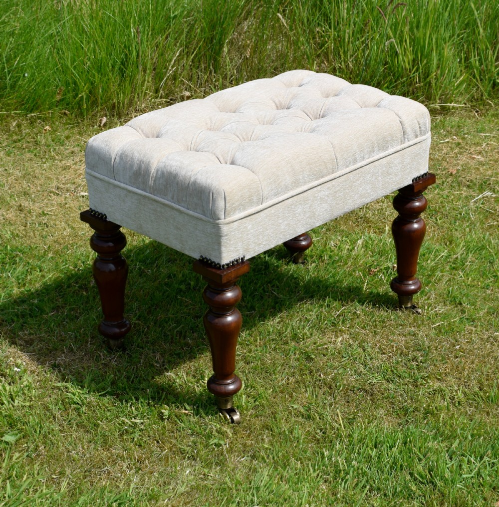 A rectangular cream fabric upholstered stool featuring deep button tufting, brass nailhead trim, and dark turned wooden legs with brass castors. View II