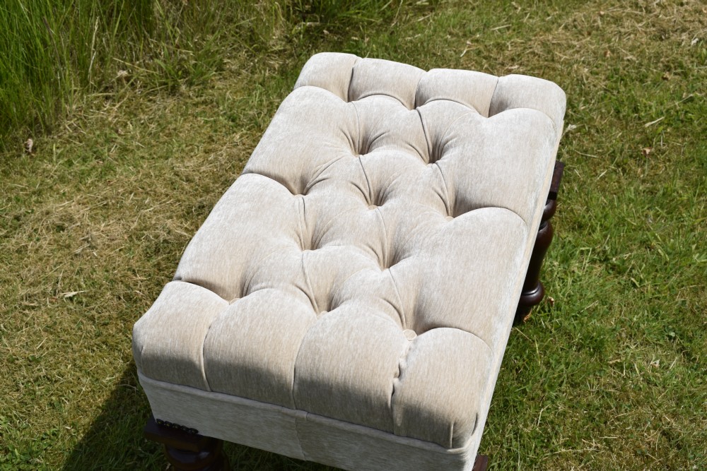 A rectangular cream fabric upholstered stool featuring deep button tufting, brass nailhead trim, and dark turned wooden legs with brass castors. View III