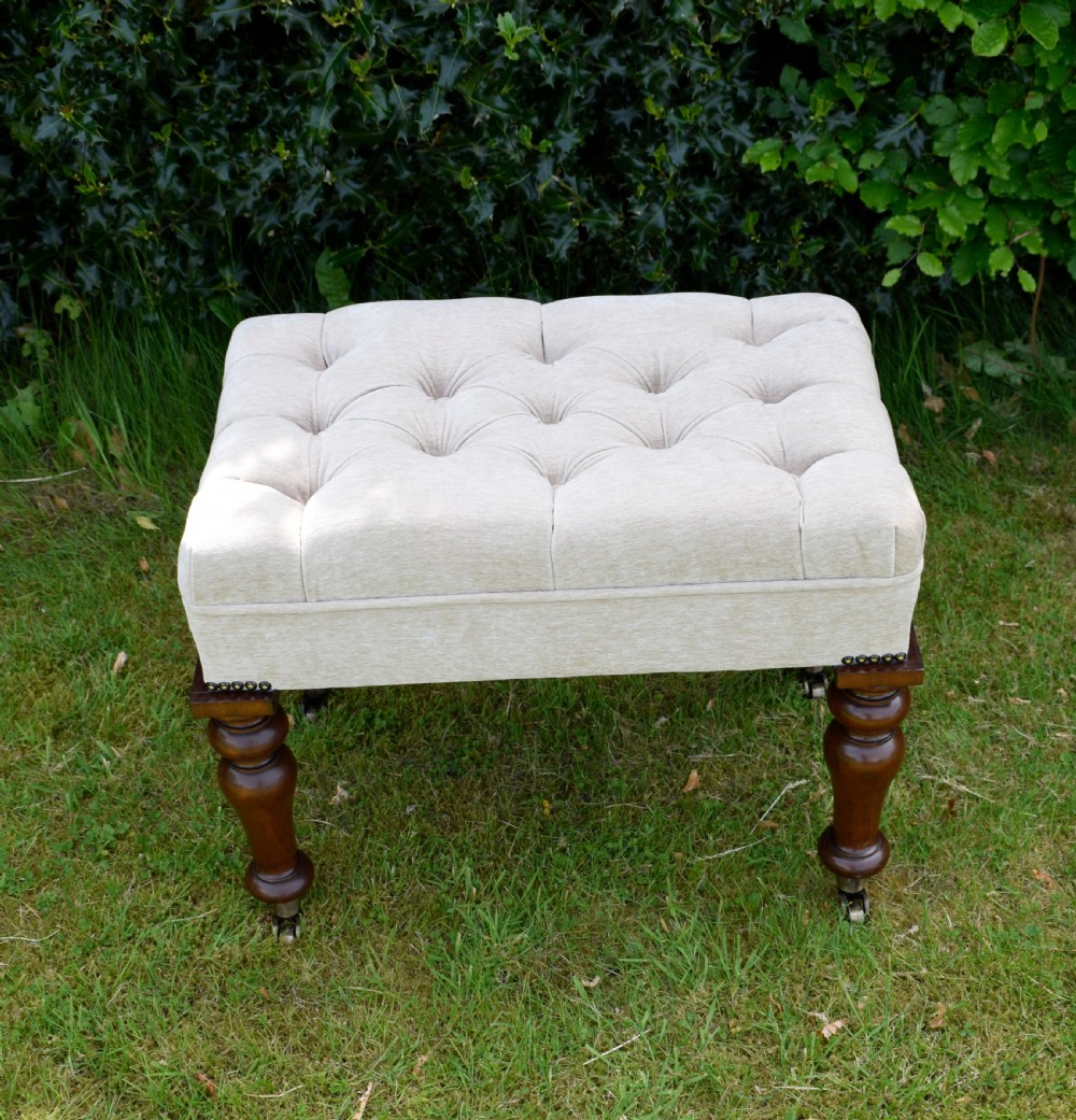 A rectangular cream fabric upholstered stool featuring deep button tufting, brass nailhead trim, and dark turned wooden legs with brass castors. View VII