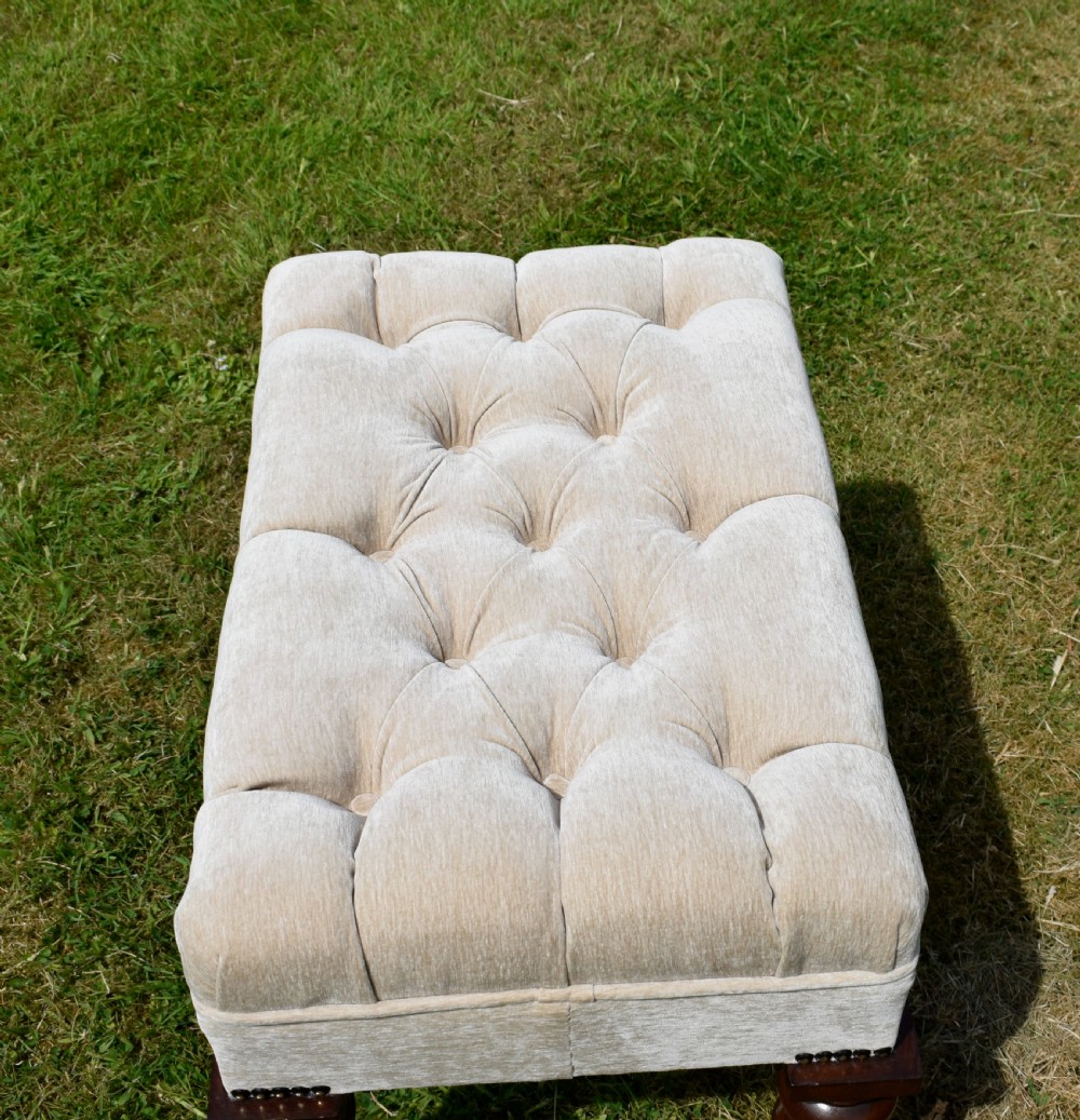 A rectangular cream fabric upholstered stool featuring deep button tufting, brass nailhead trim, and dark turned wooden legs with brass castors. View VIII