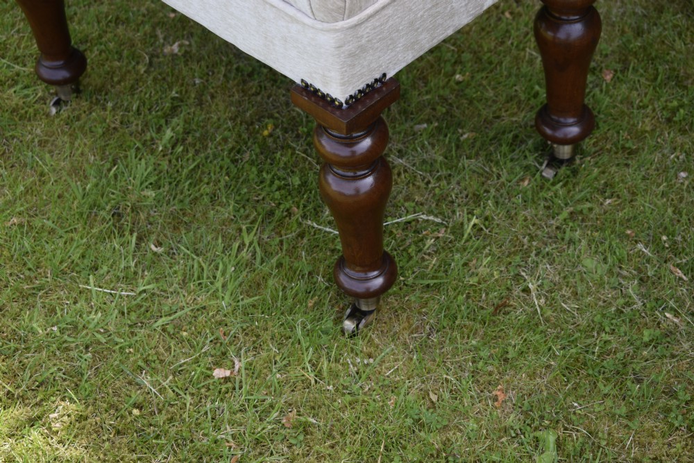A rectangular cream fabric upholstered stool featuring deep button tufting, brass nailhead trim, and dark turned wooden legs with brass castors. View IX