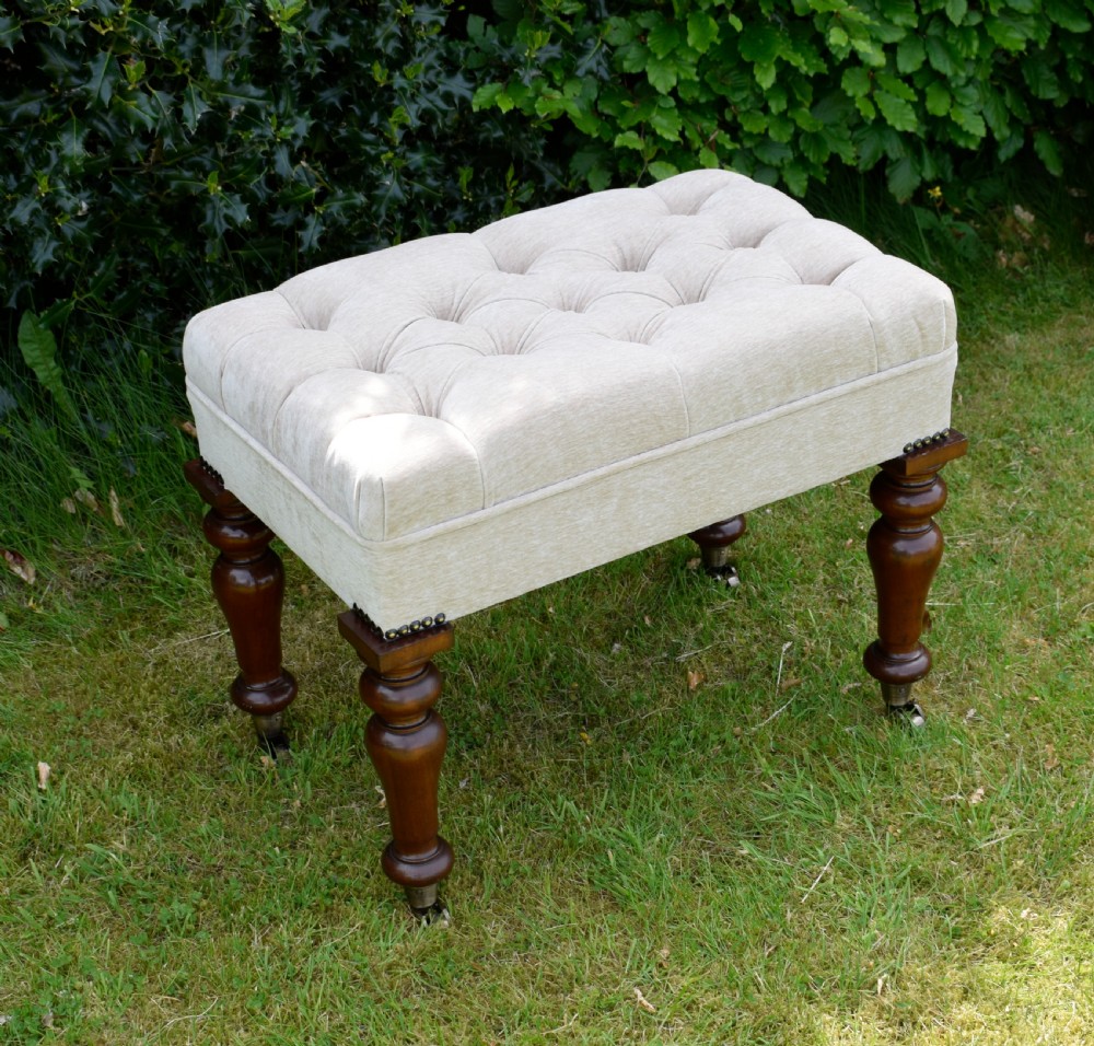 A rectangular cream fabric upholstered stool featuring deep button tufting, brass nailhead trim, and dark turned wooden legs with brass castors. View XII