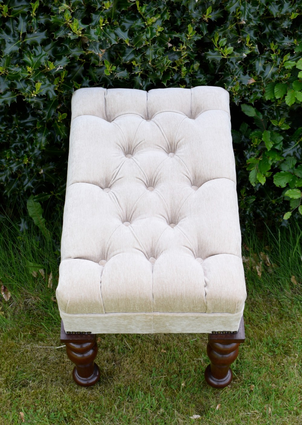 A rectangular cream fabric upholstered stool featuring deep button tufting, brass nailhead trim, and dark turned wooden legs with brass castors. View XIII