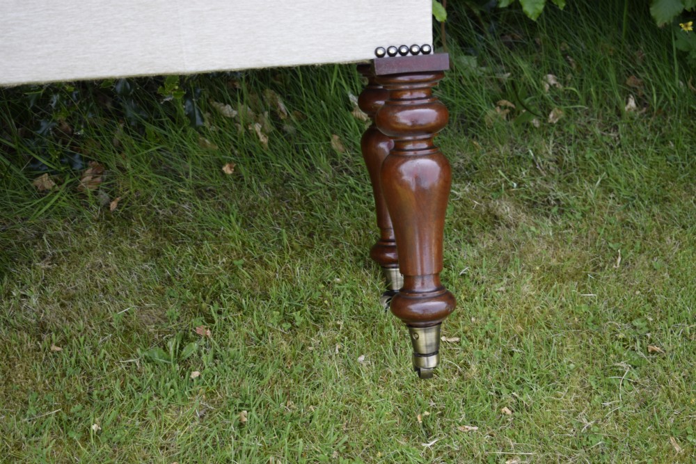 A rectangular cream fabric upholstered stool featuring deep button tufting, brass nailhead trim, and dark turned wooden legs with brass castors. View XVIII