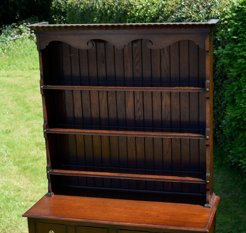 A dark oak Welsh dresser featuring an upper open plate rack with three shelves and a lower base with four drawers supported by turned legs and a bottom shelf. View VI
