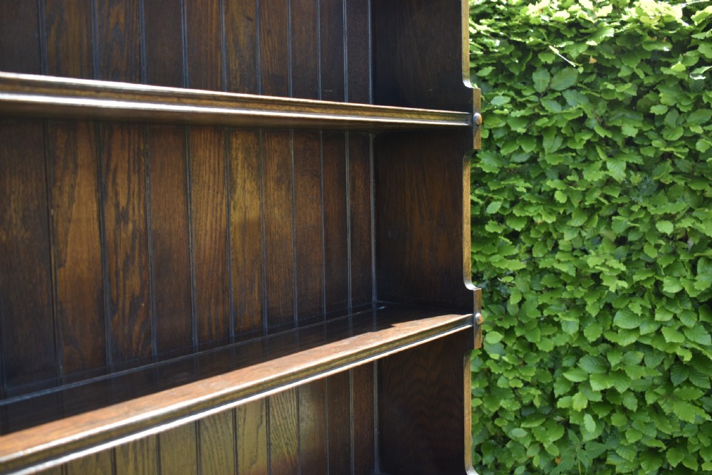 A dark oak Welsh dresser featuring an upper open plate rack with three shelves and a lower base with four drawers supported by turned legs and a bottom shelf. View IX