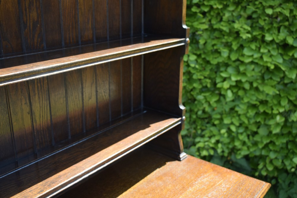 A dark oak Welsh dresser featuring an upper open plate rack with three shelves and a lower base with four drawers supported by turned legs and a bottom shelf. View X