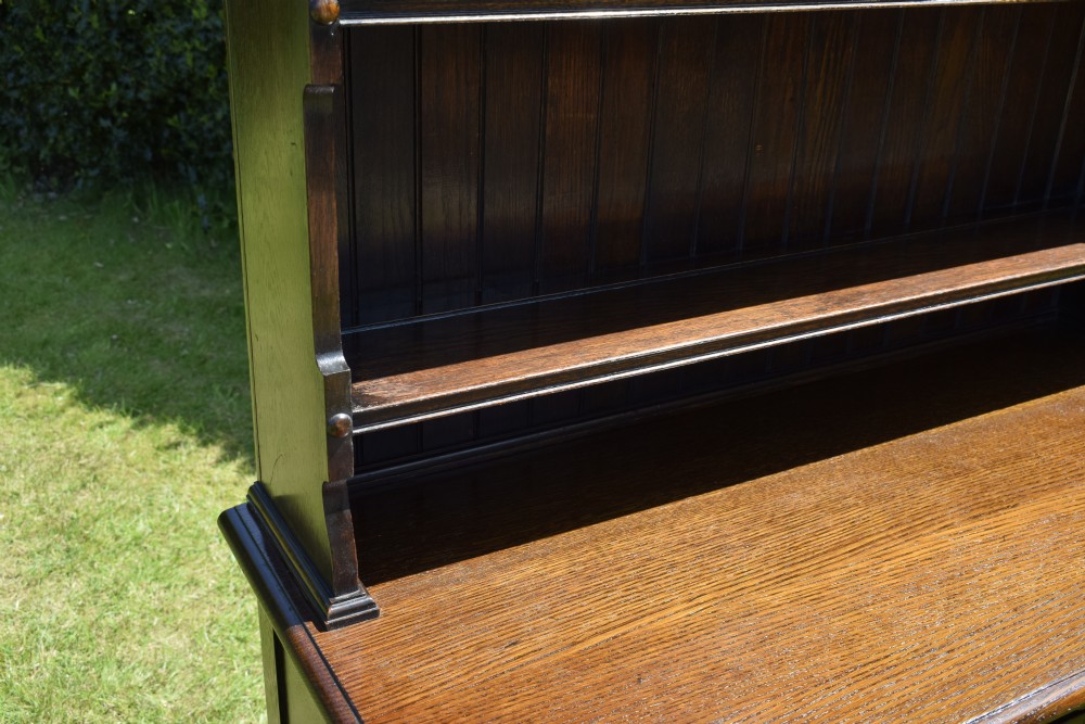A dark oak Welsh dresser featuring an upper open plate rack with three shelves and a lower base with four drawers supported by turned legs and a bottom shelf. View XII