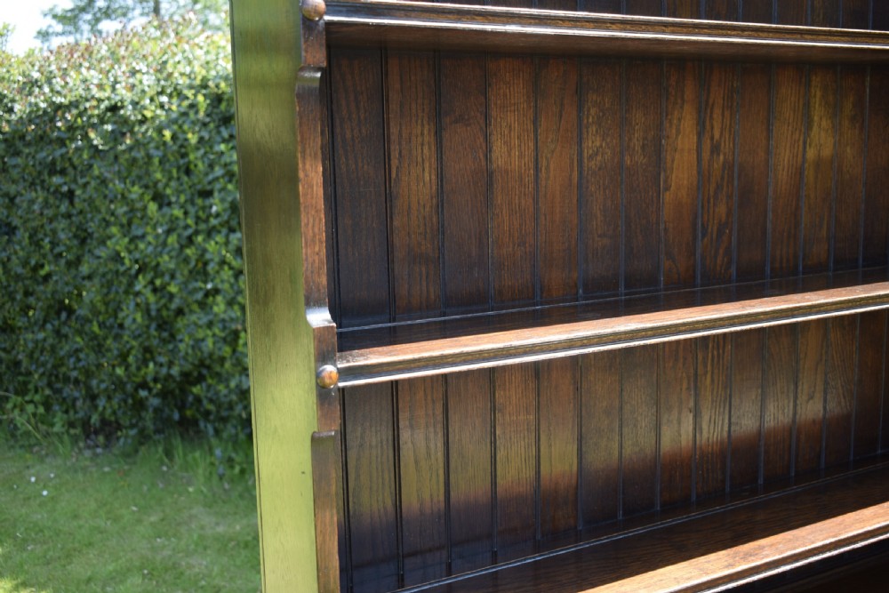A dark oak Welsh dresser featuring an upper open plate rack with three shelves and a lower base with four drawers supported by turned legs and a bottom shelf. View XIII