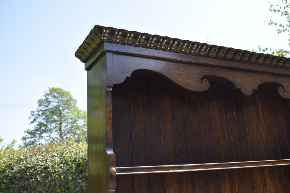 A dark oak Welsh dresser featuring an upper open plate rack with three shelves and a lower base with four drawers supported by turned legs and a bottom shelf. View XIV