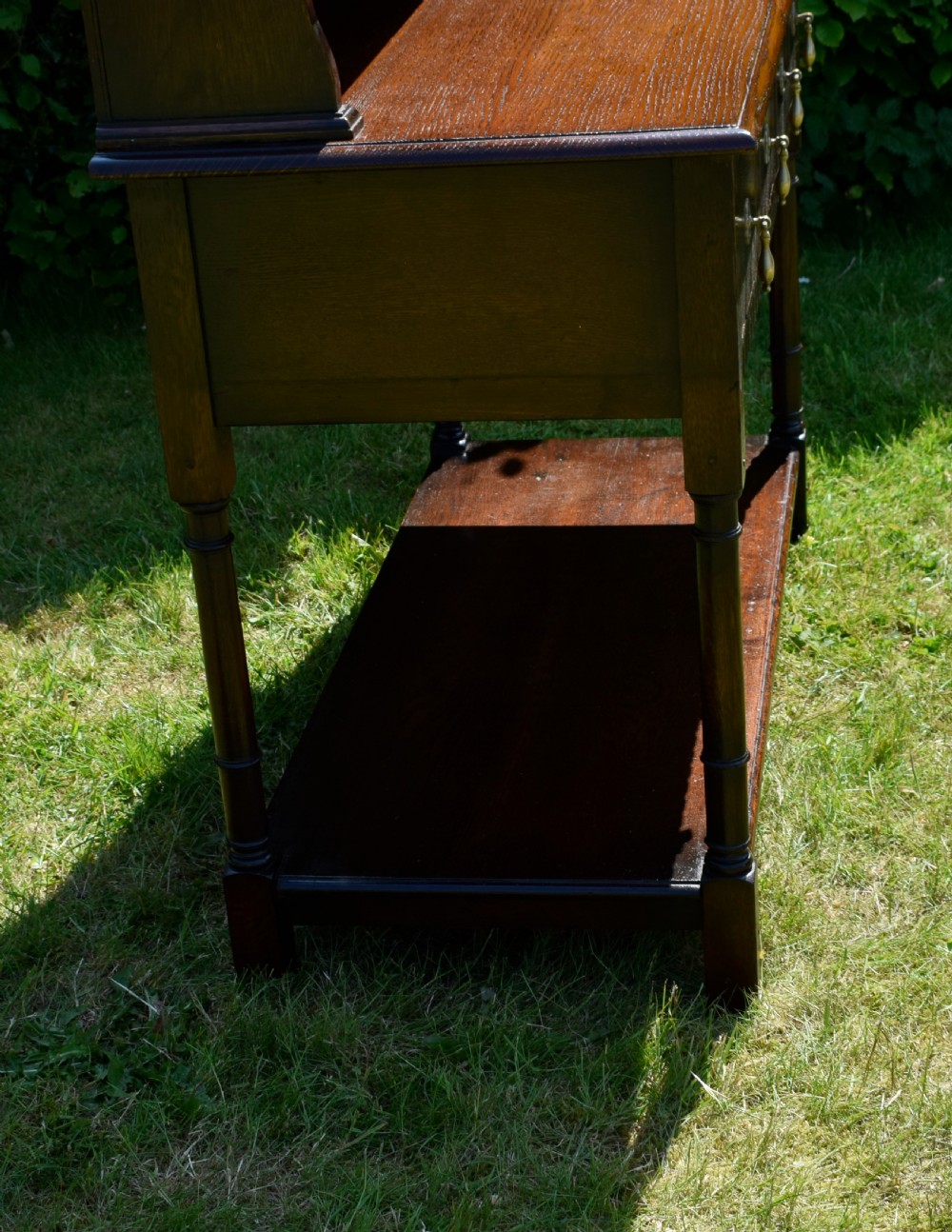 A dark oak Welsh dresser featuring an upper open plate rack with three shelves and a lower base with four drawers supported by turned legs and a bottom shelf. View XVI