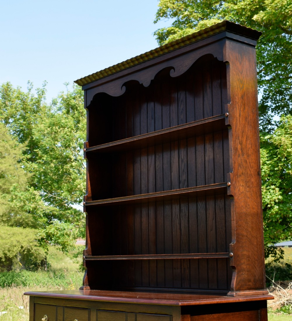 A dark oak Welsh dresser featuring an upper open plate rack with three shelves and a lower base with four drawers supported by turned legs and a bottom shelf. View XX