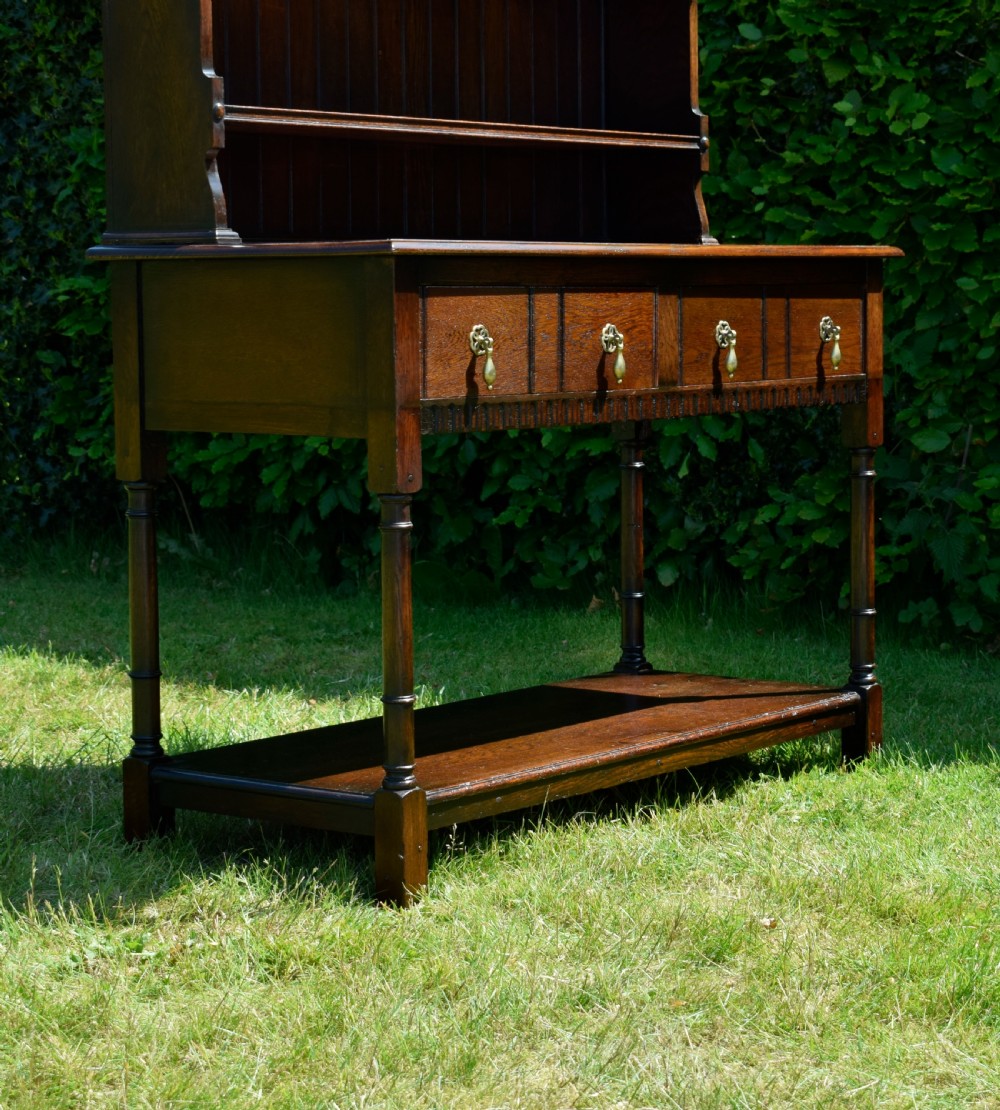 A dark oak Welsh dresser featuring an upper open plate rack with three shelves and a lower base with four drawers supported by turned legs and a bottom shelf. View XXV