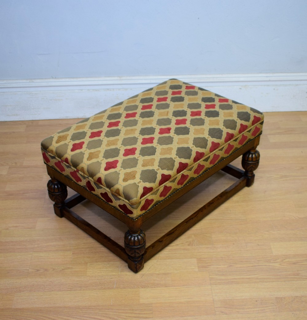 An antique carved oak stool with a geometric patterned upholstered seat, turned legs, and a perimeter wood stretcher.
