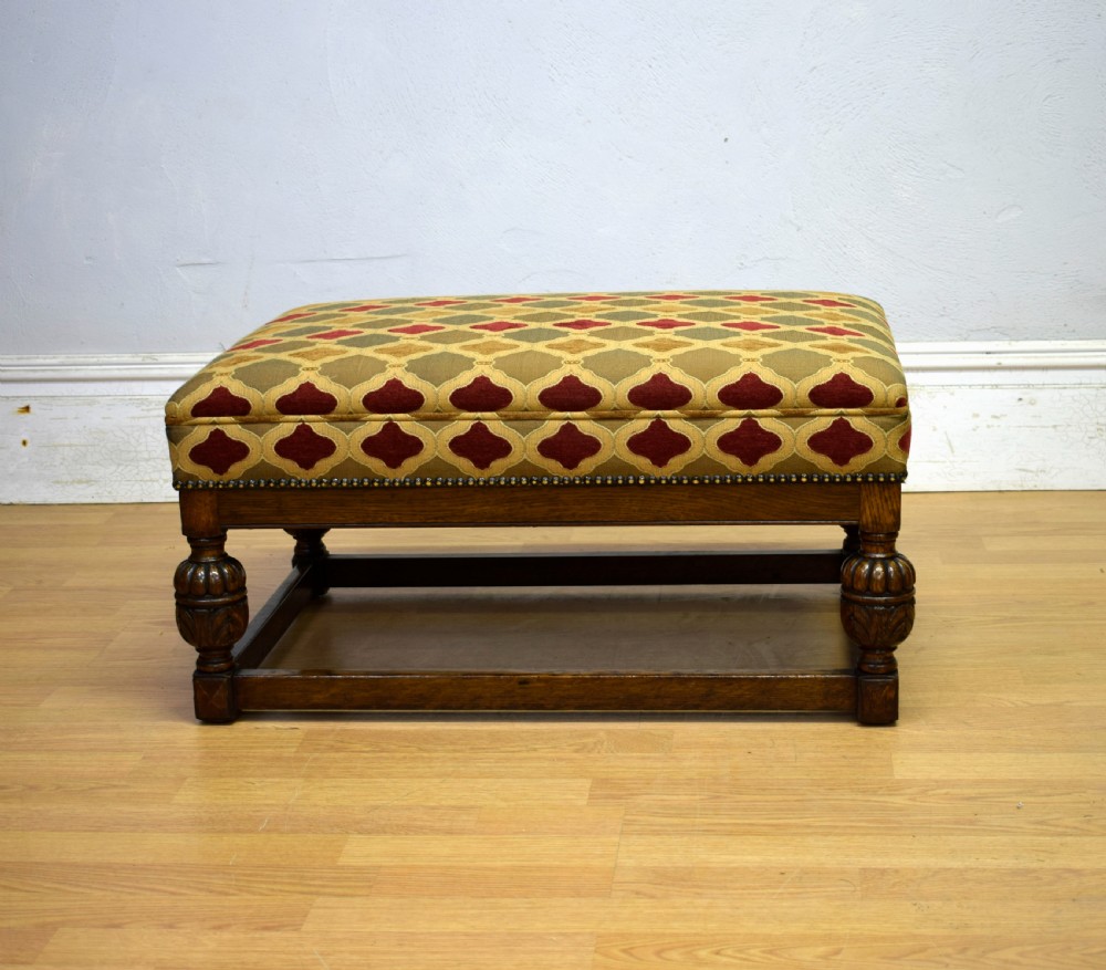 An antique carved oak stool with a geometric patterned upholstered seat, turned legs, and a perimeter wood stretcher. View V