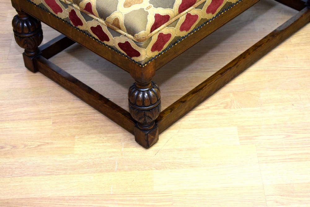 An antique carved oak stool with a geometric patterned upholstered seat, turned legs, and a perimeter wood stretcher. View VII