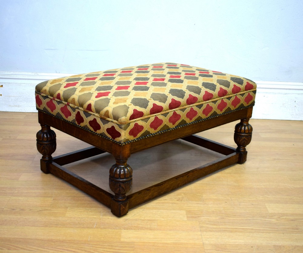 An antique carved oak stool with a geometric patterned upholstered seat, turned legs, and a perimeter wood stretcher. View X