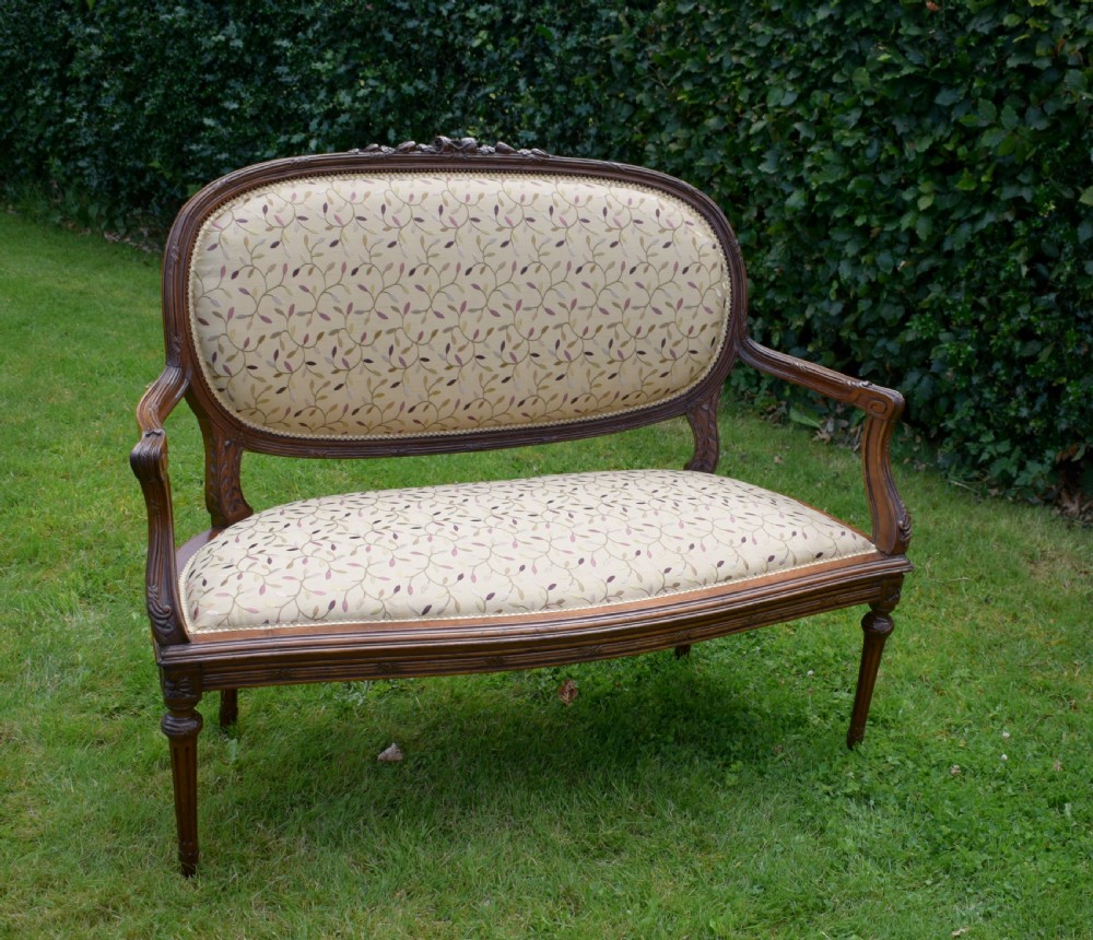 A French carved walnut settee with an oval upholstered backrest, turned fluted legs, and patterned textile upholstery. View II