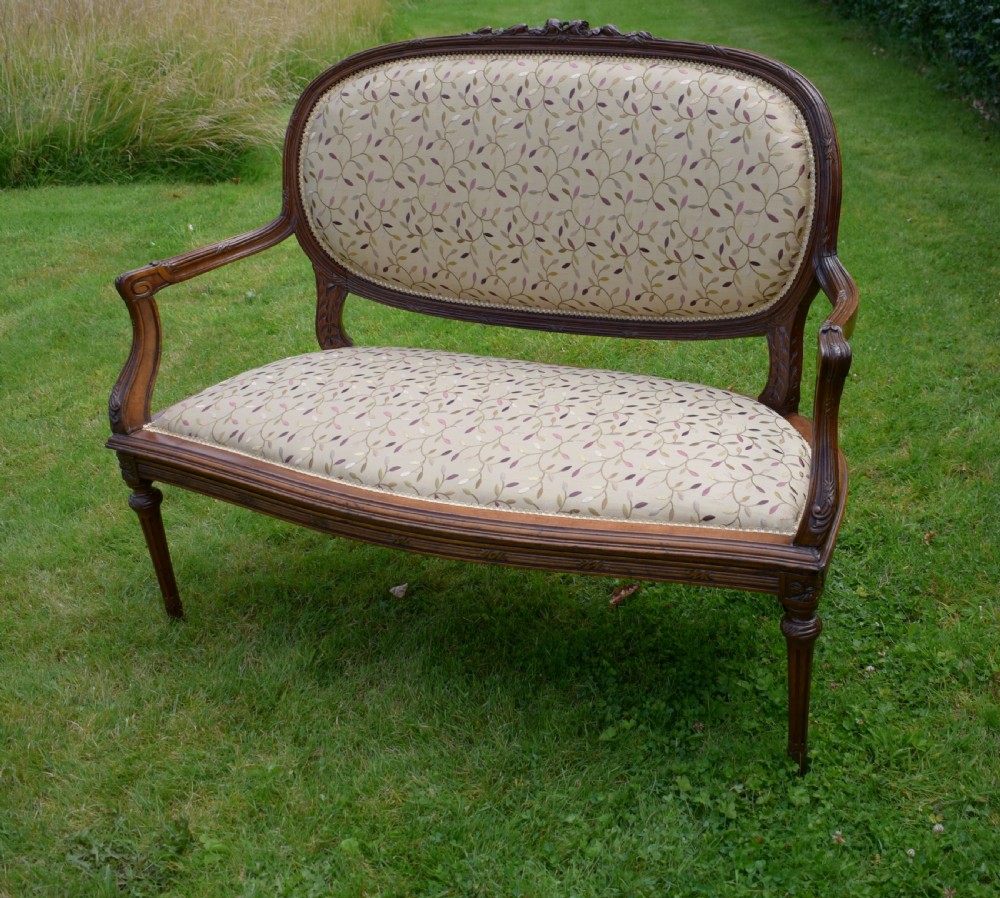 A French carved walnut settee with an oval upholstered backrest, turned fluted legs, and patterned textile upholstery. View V
