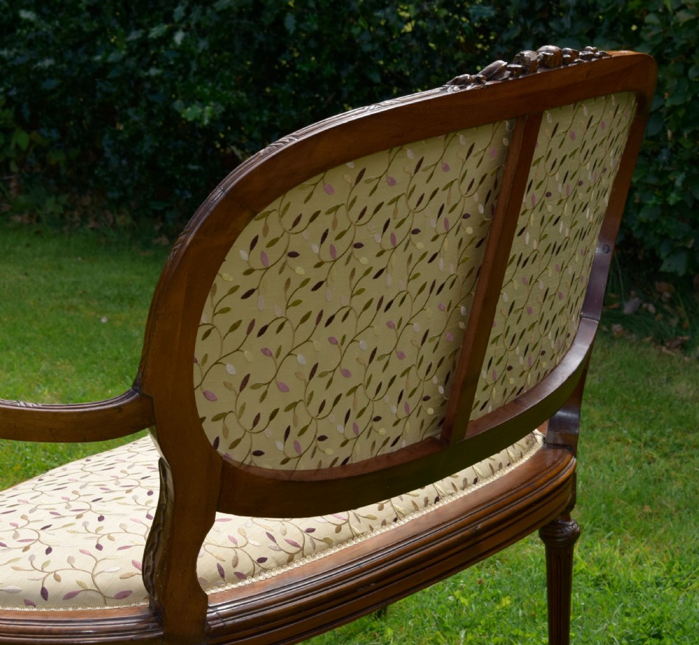 A French carved walnut settee with an oval upholstered backrest, turned fluted legs, and patterned textile upholstery. View XXI