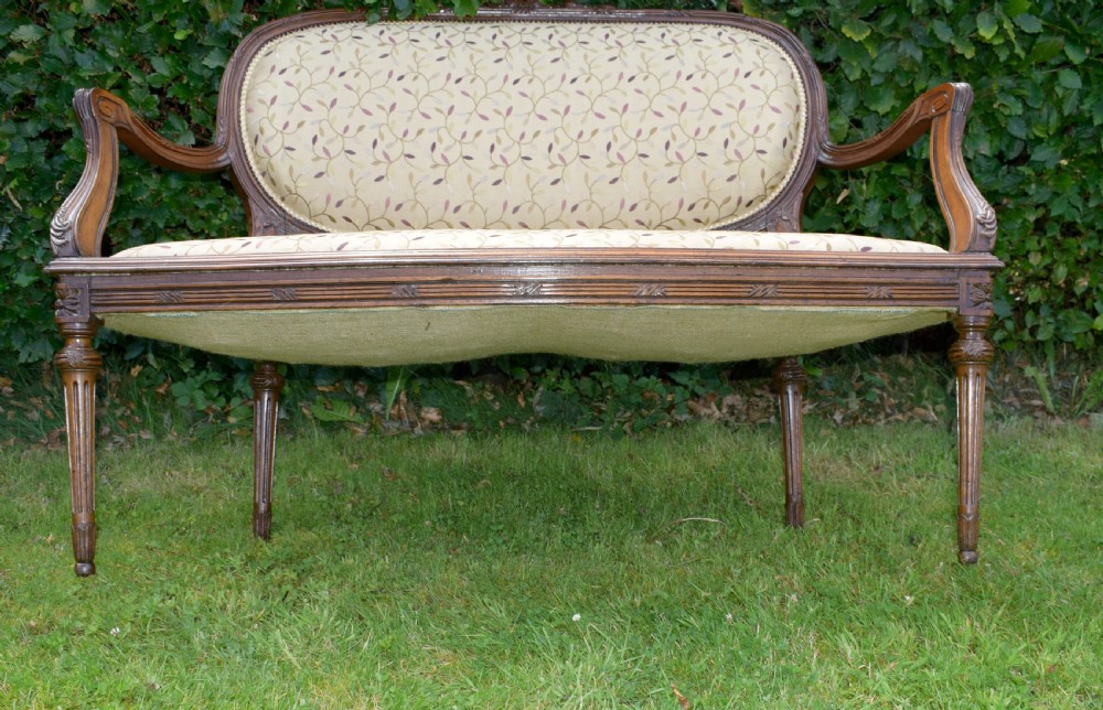 A French carved walnut settee with an oval upholstered backrest, turned fluted legs, and patterned textile upholstery. View XXIV