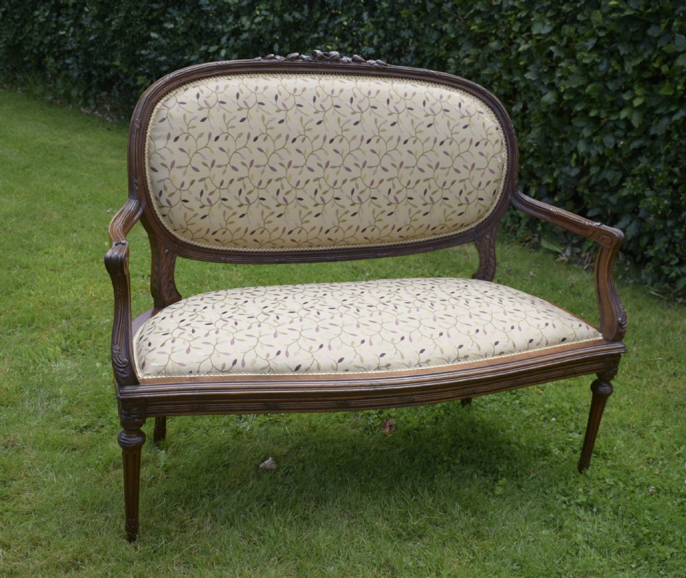 A French carved walnut settee with an oval upholstered backrest, turned fluted legs, and patterned textile upholstery.