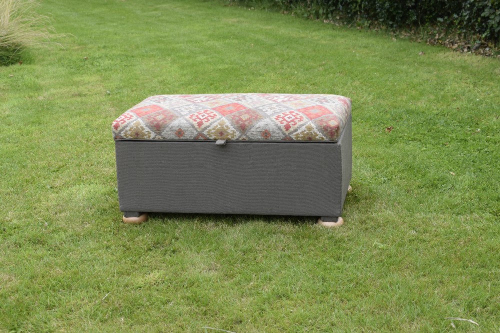 A rectangular upholstered storage ottoman featuring a dark grey base, short turned wooden feet, and a geometric kilim-patterned hinged top. View II