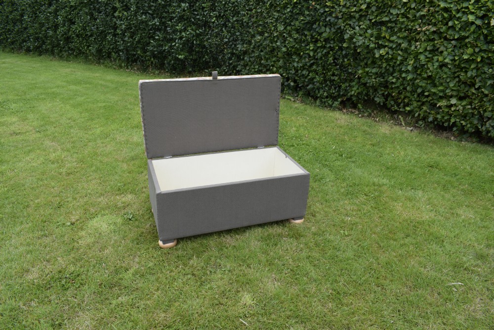 A rectangular upholstered storage ottoman featuring a dark grey base, short turned wooden feet, and a geometric kilim-patterned hinged top. View VIII