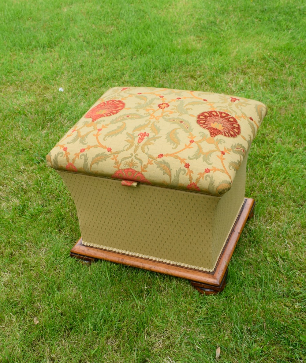 A square William IV upholstered ottoman work box featuring a gold and red floral patterned lid, flared fabric body, and a mahogany plinth base.