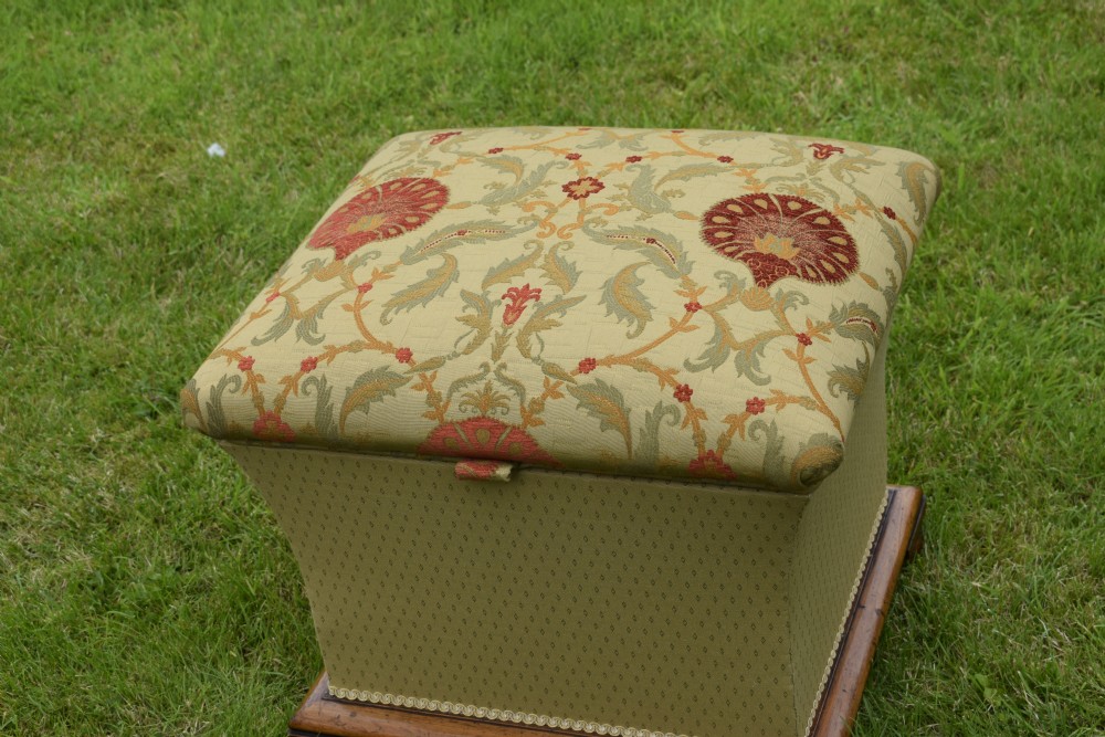 A square William IV upholstered ottoman work box featuring a gold and red floral patterned lid, flared fabric body, and a mahogany plinth base. View III