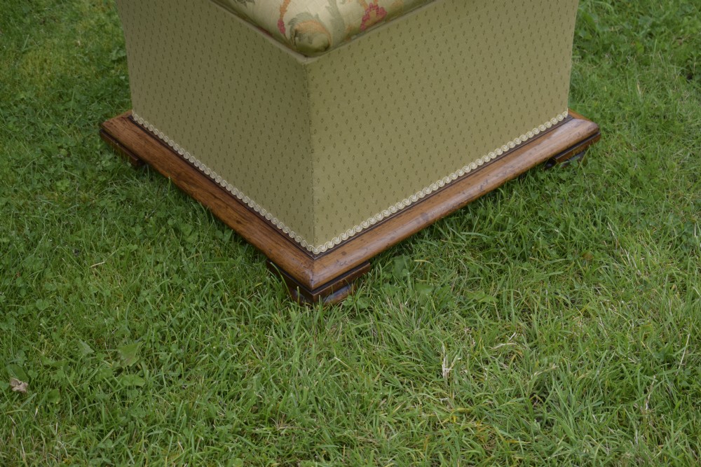 A square William IV upholstered ottoman work box featuring a gold and red floral patterned lid, flared fabric body, and a mahogany plinth base. View X