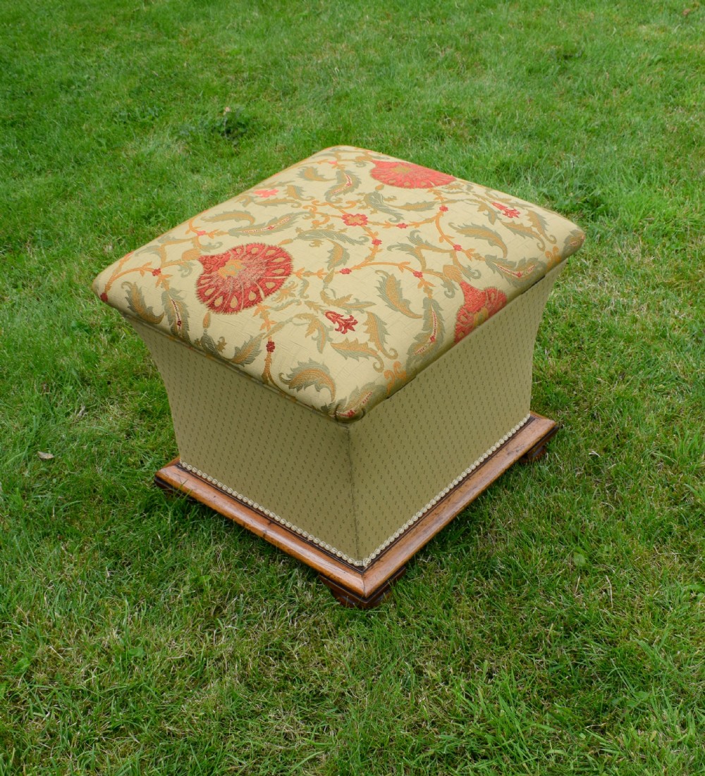 A square William IV upholstered ottoman work box featuring a gold and red floral patterned lid, flared fabric body, and a mahogany plinth base. View XVI